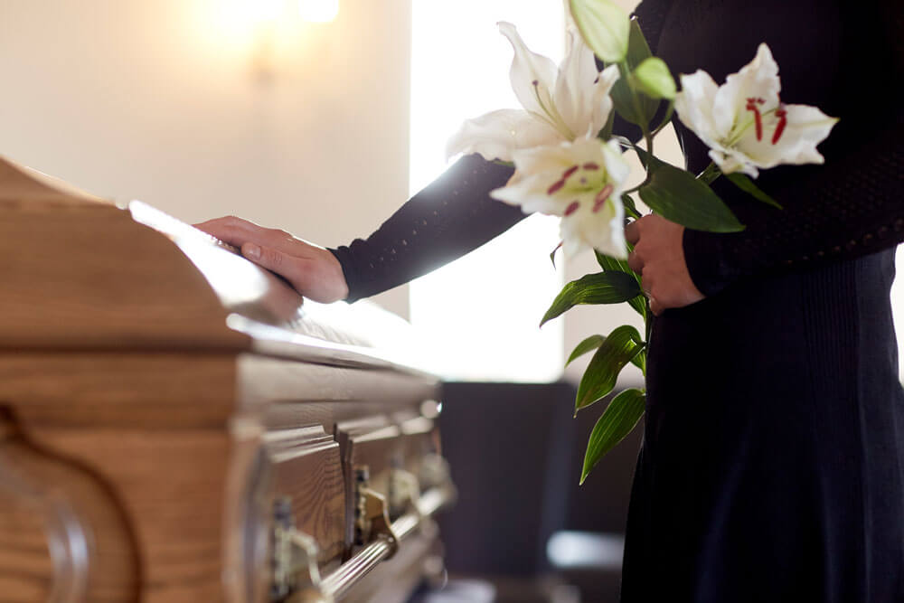Frau mit Lilienblumen und Sarg bei Beerdigung