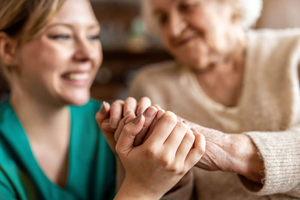 einer älteren Frau, die mit einer Krankenschwester Händchen hält