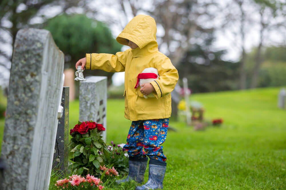 Trauriges kleines Kind, blonder Junge, der im Regen auf dem Friedhof steht, trauriger Mensch, trauernd